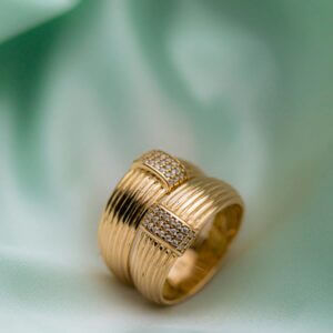 Close-up of a luxury gold ring with diamonds on a soft green fabric surface.